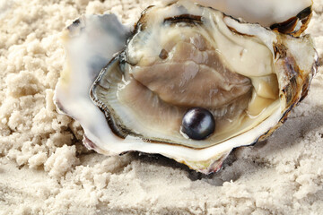 Open oyster with black pearl on sand, closeup