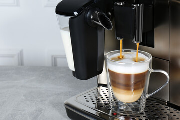 Modern coffee machine making latte into glass cup on grey table, closeup. Space for text