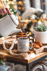 Lifestyle. A woman pours tea from a teapot during the Christmas holidays. The inscription on the mug in Russian: do what you want. Still-life. The concept of home warmth, comfort.