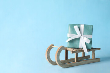 Wooden sleigh with Christmas gift box on light blue background, space for text