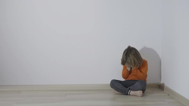 Hand shadow pointing with finger reflected on wall threatening scared child sitting in a corner, loneliness and bad and fearful  education education concept,  blond hair boy  is crouched in a corner
