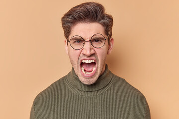 Portrait of outraged young European man screams angrily keeps mouth opened expresses negative...