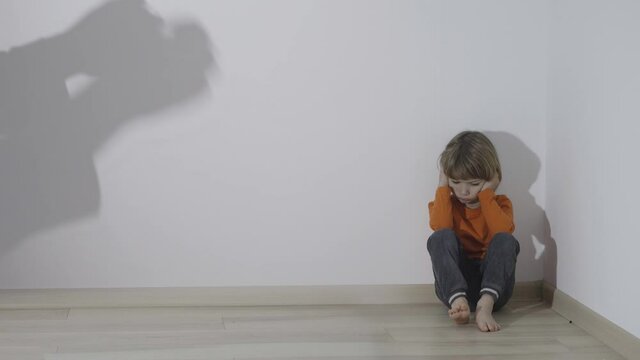 Wall reflected shadows of parent hands aggressive gestures over squatting lonely child in the corner of his room, concept of emotional abuse and domestic violence
