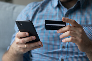 Close up male hands holding cellphone using debit card buying on internet, makes on-line shopping. E-commerce retail services client, funds transfer, spend money through electronic commerce concept
