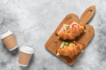 Croissant sandwich and coffee in a paper cup, gray grunge background. Croissants with ham and fresh...