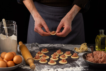 A man imposes minced meat on prepared round forms of dough, the process of preparing a traditional Russian dish dumplings