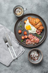 Croissant sandwich with fried egg and bacon, a cup of coffee, cherry tomato, microgreens. Tasty breakfast. Top view, flat lay.