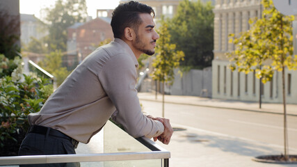 Side view portrait relaxed hispanic business man standing at railing modern skyscraper office...