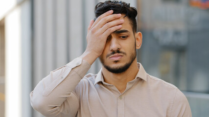 Outdoors male portrait sad hispanic latin man young bearded guy upset frustrated stressful feeling desperate businessman looking at camera close face with hand palm lost loosing problem trouble