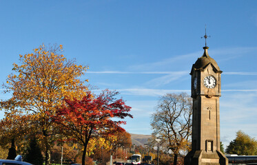 Fototapeta na wymiar Isolated Stone Clock Tower & Tree with Golden Autumn Leaves against Blue Sky