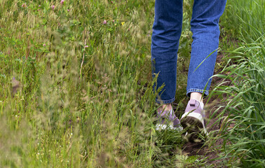 selective focus on legs of  teenage girl in jeans and purple sneakers on  meadow. Concept of loneliness and communication with nature