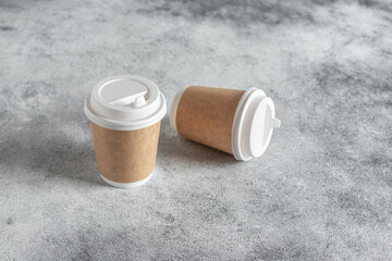 Paper cup for coffee on a gray concrete grunge background. Side view, selective focus. Disposable tableware.