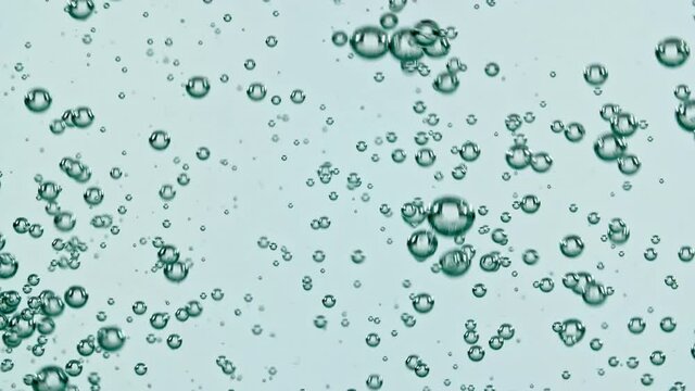Macro shot of air bubbles in water rising up on light blue background. Slow motion. High quality FullHD footage