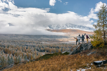 Four people tourists stand against the background of a snow-covered forest and mountains