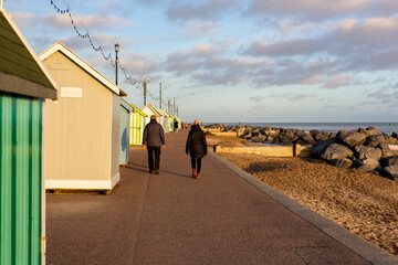 Beach huts in Felixstowe, Suffolk, England with an unknown elderly couple walking away from camera