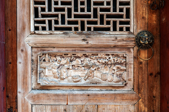 Close-up detail of ancient classic wooden door panel decorated with typical Chinese architecture style pattern and woodcarving with old metal doorknob installed at an old house in China