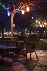Illuminated Tree and tables, chairs, garden equipment under it and city light at background