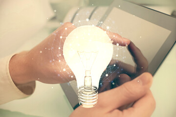 Double exposure of man's hands holding and using a digital device and bulb hologram drawing. Idea concept.