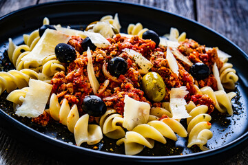 Fusilli with minced meat, tomato sauce, parmesan cheese and olives served on wooden table
