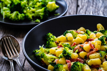 Gnocchi with bacon and broccoli on wooden table
