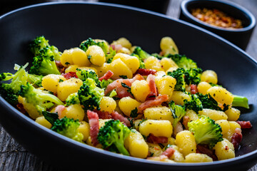 Gnocchi with bacon and broccoli on wooden table
