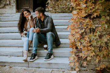 Obraz na płótnie Canvas Young couple sitting on outdoor stairs on a autumn day and using mobile phone