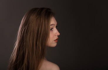 Rear view of a young blonde woman with long hair. Female looking to side isolated on dark background copy space. Beautiful and healthy hair, care and coloring.