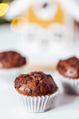 Chocolate cupcakes or muffins with Ginger house and Christmas lights from Christmas tree in blurry background. Festive and holiday decoration