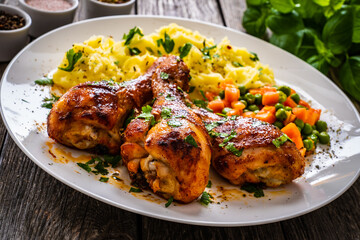 Barbecue chicken drumsticks with potato puree, grean peas and carrot on wooden table
