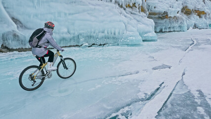 Woman is riding bicycle near the ice grotto. The rock with ice c