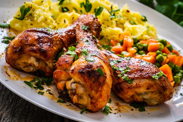 Barbecue chicken drumsticks with potato puree, grean peas and carrot on wooden table
