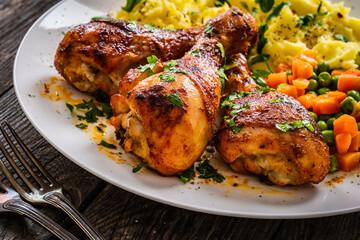 Barbecue chicken drumsticks with potato puree, green peas and carrot on wooden table