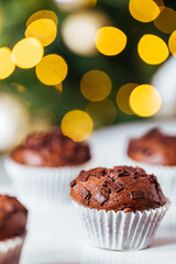 Chocolate cupcakes or muffins with Ginger house and Christmas lights from Christmas tree in blurry background. Festive and holiday decoration