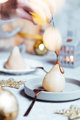 Cooked pear poached with melting chocolate served as dessert to celebrate Christmas or New year. Decorated in holiday spirit and mood with lot of decoration and lights