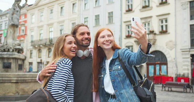 Three male and female best friends shooting video on smartphone in city. Young students taking selfie photo, smiling and laughing. Technology, friendship, gadgets concept.