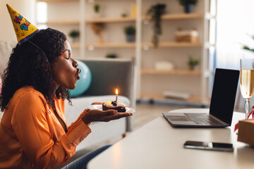 African Lady At Laptop Blowing Candle On B-Day Cake Indoor