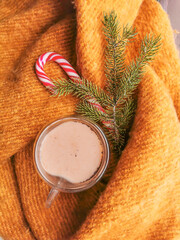 Cozy winter day with ginger wool scarf and glass cup of hot coffee and christmas candy.