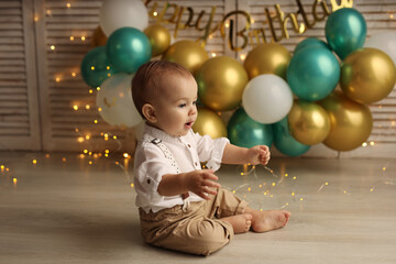 Cute blond kid in a festive shirt and trousers. Happy baby on the background of balloons with garlands and the inscription happy birthday. High-quality photography