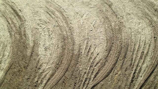 AERIAL VIEW: Pattern on the ground of repetitive arcing traces of a tractor wheel tread on agricultural land when plowing the soil. Agribusiness concept.