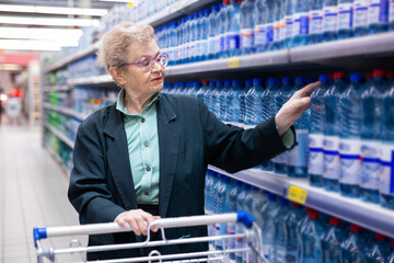 elderly woman with glasses selects bottled water in the department of supermarket