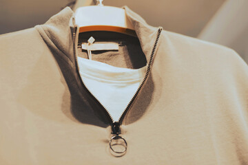  A set of a white T-shirt and a beige polo with a zipper collar hangs on a white hanger in a clothing store. Shopping. ©  Valeri Vatel