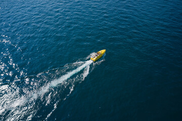 High-speed luxury yellow boat with people moving on dark blue water. Boat performance movement on the water aerial view.