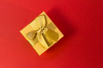 Closed golden gift box with silk gold ribbon bow on bright pink background