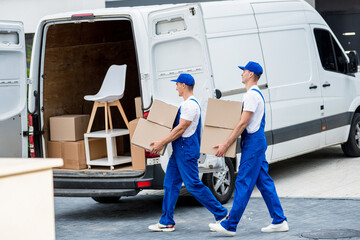 Two removal company workers are loading boxes and furniture into a minibus.