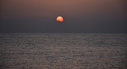 The sun rises over the sea from behind the mountains. ripples on the surface of the water. Dawn in dark colors