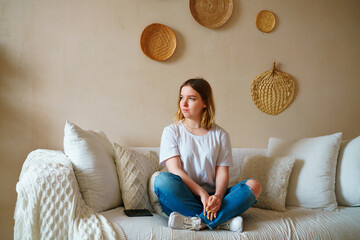 Stressed young woman sitting on sofa in casual clothes, worrying about problems alone at home,...