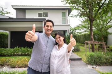 Happy Asian couple with thumb up standing together in front of thier house