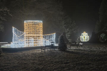 Świąteczna iluminacja w parku dworskim w mieście Iłowa w Polsce. Jest zimowa noc, widok jest lekko rozmyty z powodu intensywnych opadów śniegu.