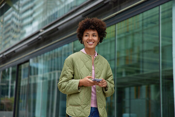 Positive young woman with happy smile on face uses navigation app on mobile phone enjoys travel...