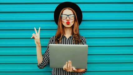Portrait of stylish young woman with laptop on blue background
